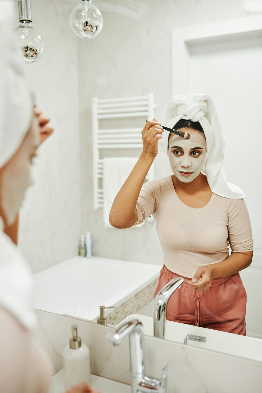 Woman applying Dead Sea mud mask with natural soap on towel beside her