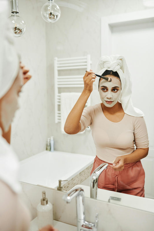 Woman applying Dead Sea mud mask with natural soap on towel beside her