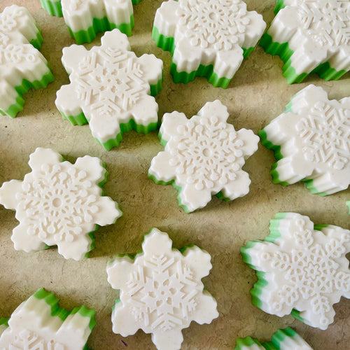 Snowflake-shaped cookies with green and white icing on a baking sheet.